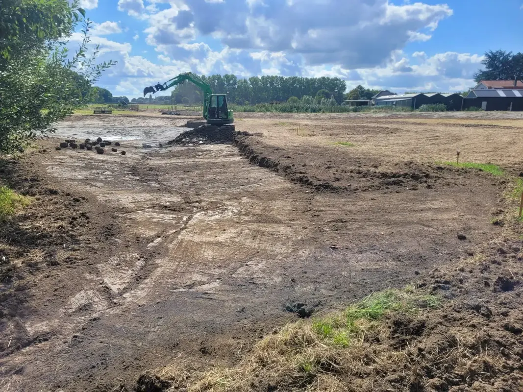 Rupsgraafmachine graaft een sleuf in open terrein, met uitgezette piketpaaltjes langs het werkvak